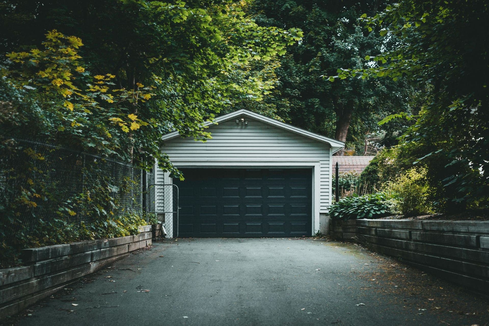 Asphalt driveway between timber retaining walls leading to a detached garage