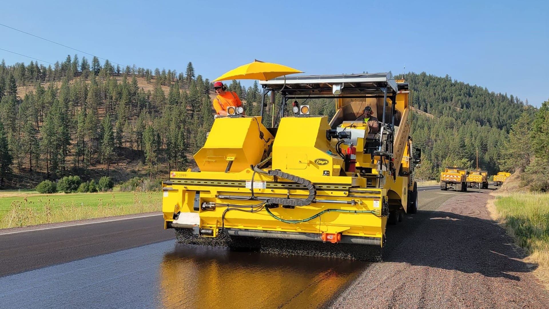 Yellow paving machine resurfacing a rural two-lane road